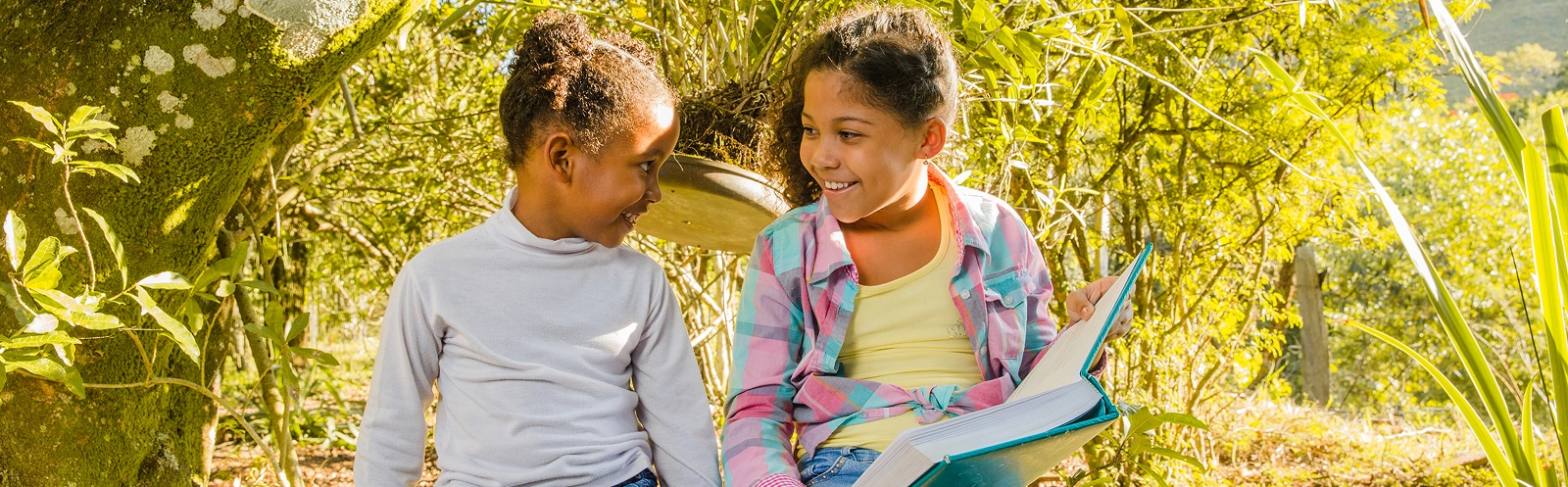 young-sisters-with-book-sitting-tree